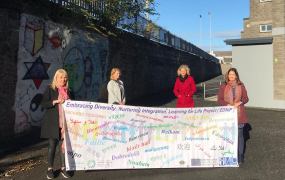 Four women holding a banner on the grounds of a school.