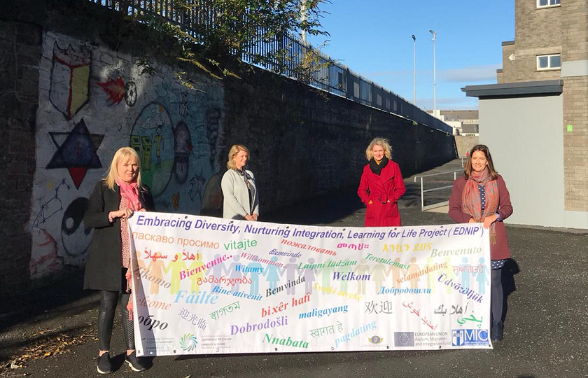 Four women holding a banner on the grounds of a school.